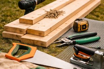 Holzbretter, Schrauben und Werkzeug für den Bau eines Hochbeets im Garten