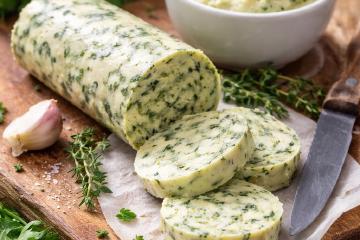Selbstgemachte Kräuterbutter mit frischen Gartenkräutern auf einem Holzbrett